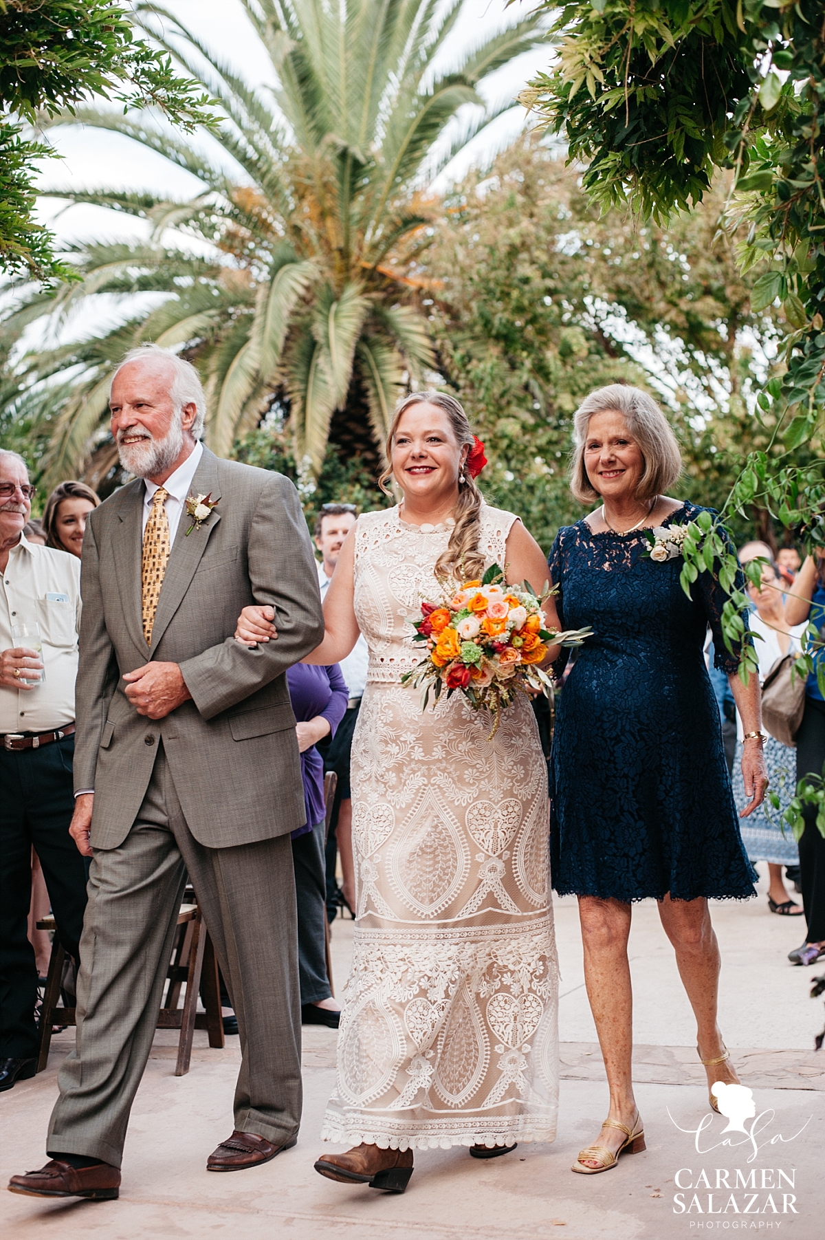 Beaming Winters bride walking the aisle with both parents - Carmen Salazar