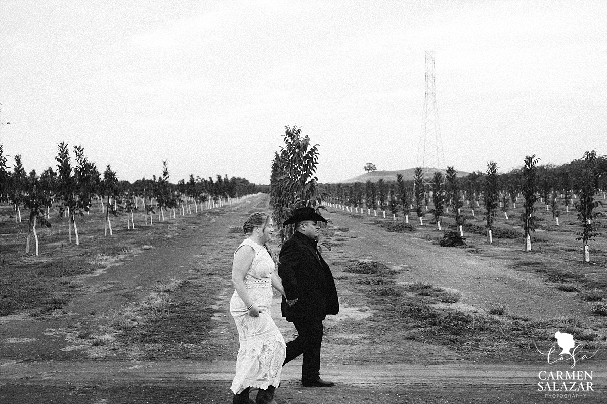 Bride and groom walking along orchards to reception - Carmen Salazar