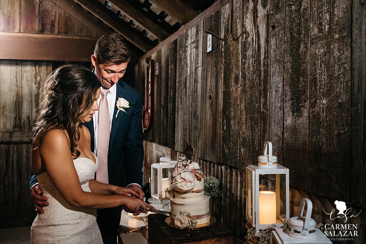 Bride and groom cutting cake in rustic barn - Carmen Salazar 