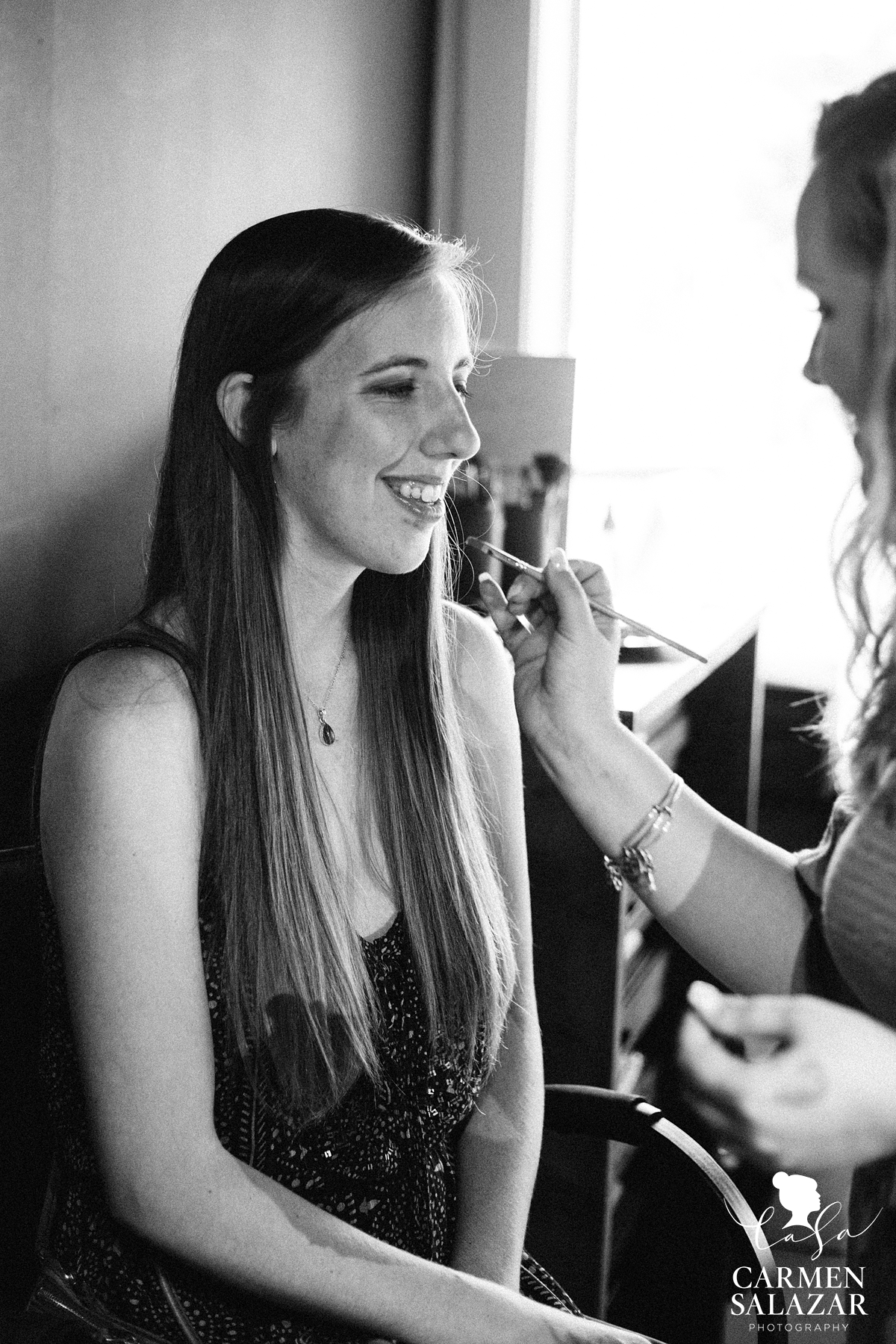 black and white photograph of woman smiling applying makeup