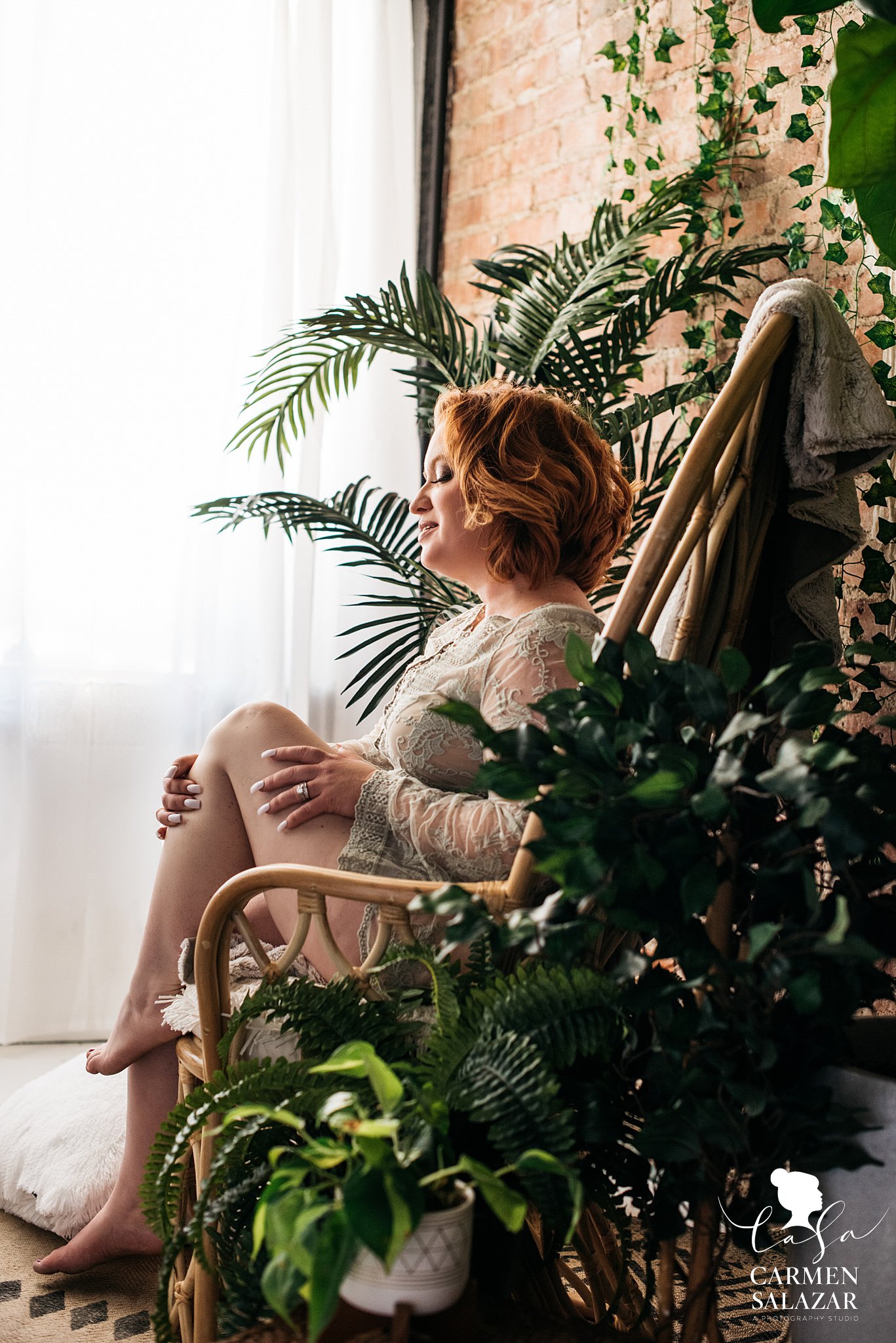 Soft light boudoir picture of a beauty sitting on a chair with greenery around 